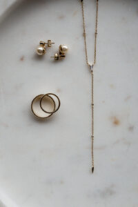 Necklace, pearl earrings, and wedding rings beautifully arranged on a marble surface