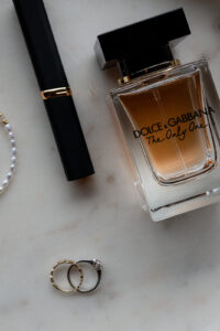 Flat lay of perfume, lipstick, and a wedding ring on a marble background