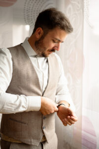 Mid-shot of the groom standing by a window while fastening his wristwatch