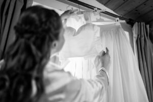 Black-and-white over-the-shoulder photo of the bride looking at her wedding dress, with focus on the gown