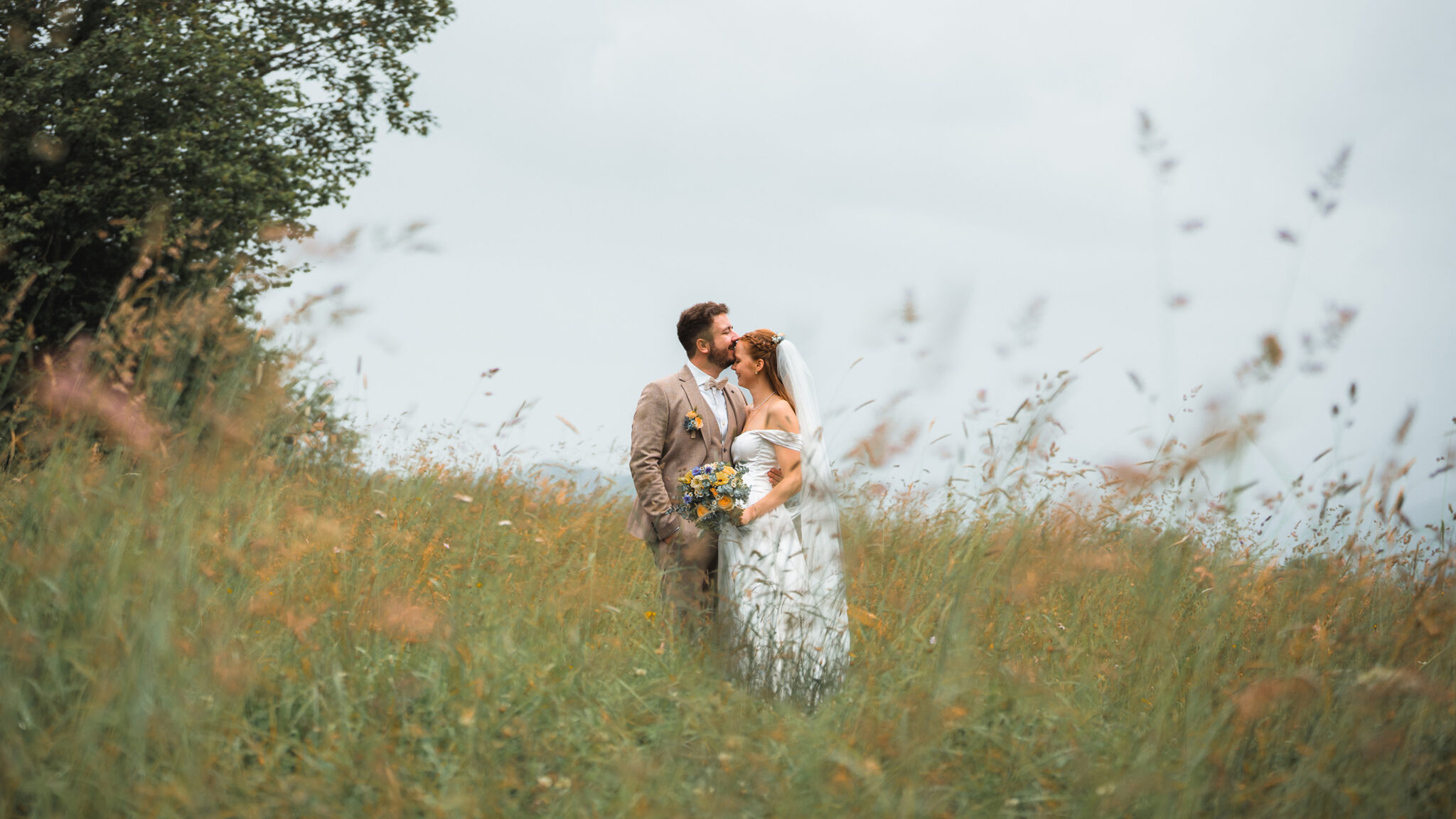 Groom kissing the bride on the forehead in a meadow with green grass and orange flowers
