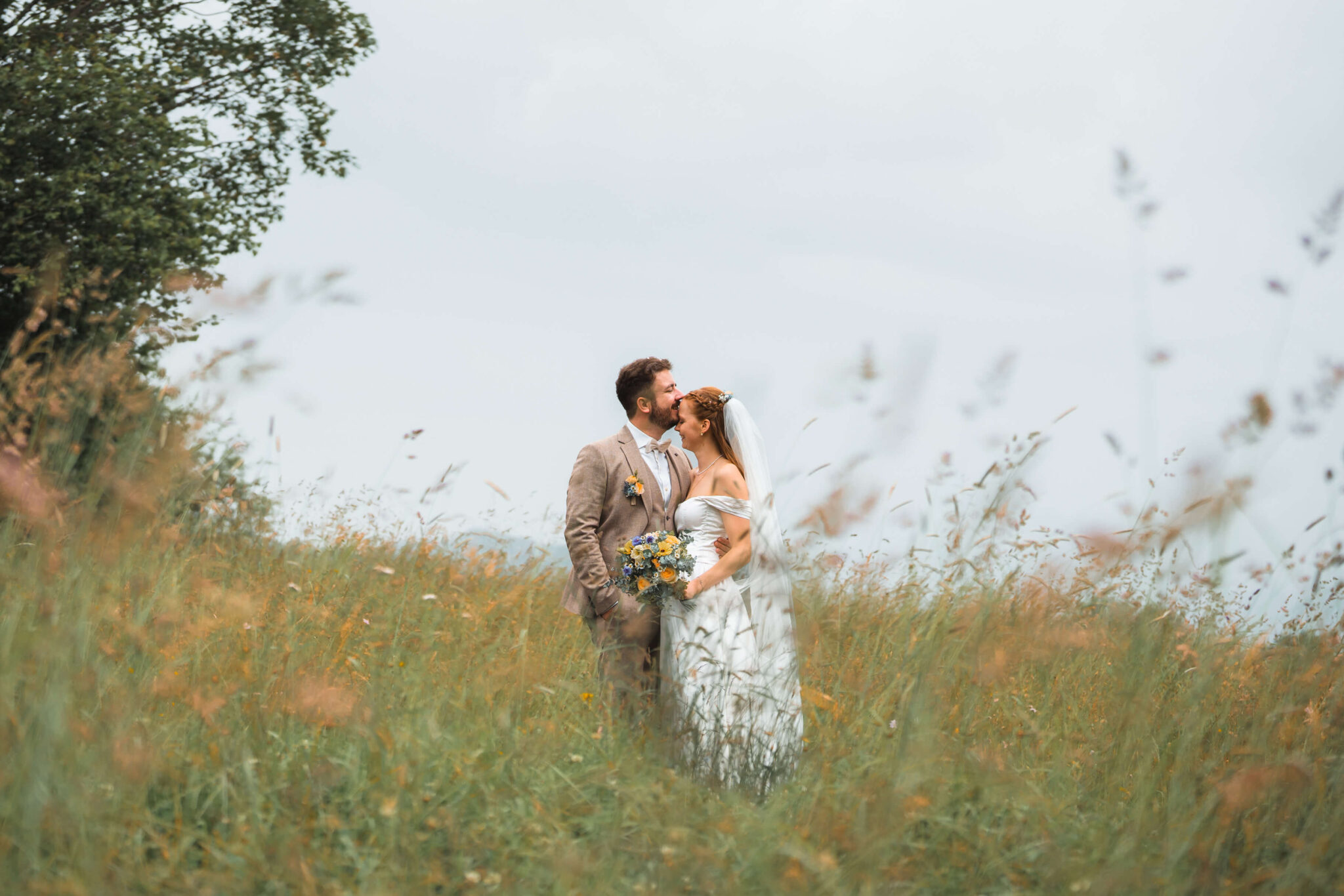 Groom kissing the bride on the forehead in a meadow with green grass and orange flowers