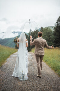 A married couple walks along a path holding up an umbrella to see if it's still raining
