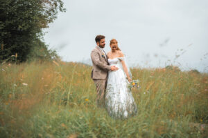 The groom holds his wife by the waist as they both look downward in a field