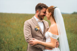Close-up of the couple standing arm in arm in a meadow with their heads together