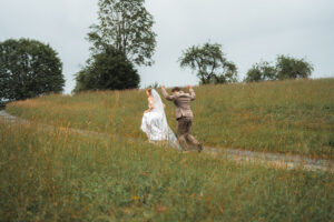 Wedding couple joyfully running up a path through tall green grass and orange flowers