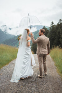 Bride and groom walk beneath a transparent umbrella, photographed from behind