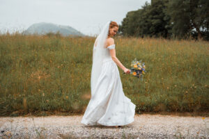 The bride twirls with her bouquet on a road beside a field, showing off her dress in motion