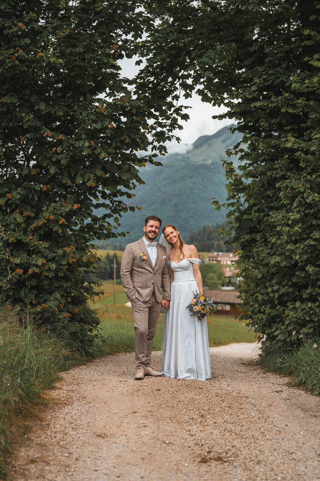 Young wedding couple holding hands and smiling at the camera beneath a hedge archway