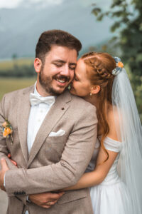 The bride hugs her husband from behind as they smile at each other over their shoulders