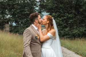 The young couple kisses in front of a hedge as the bride gently holds her husband's cheek