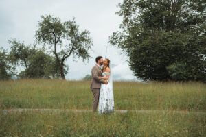 The couple embraces beneath an umbrella in a green and orange meadow