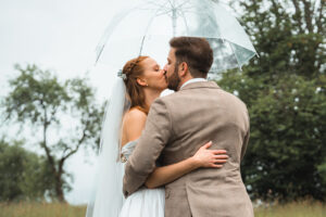 Wedding kiss beneath an umbrella with trees in the background