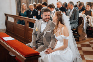 The couple smiles at each other while holding hands in front of the altar
