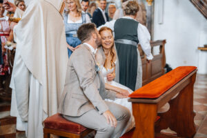 The groom kisses his bride on the cheek as they sit together before the altar