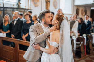 Bride and groom share a kiss in the church with their loved ones in the background