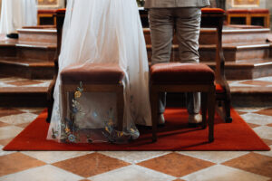 Detail shot of the bride's dress, veil, and the groom's trousers during the ceremony