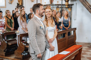 The couple holds hands during the mass while the bride looks lovingly at the groom