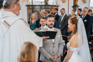 The groom reads his vows from the book held by the priest.