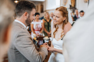 The bride places the ring on her groom's finger while smiling at him