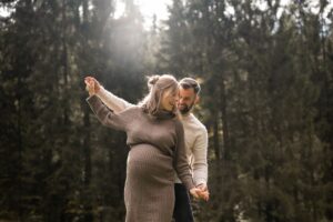 Schwangeres Paar bewegt verspielt die Arme und lacht miteinander