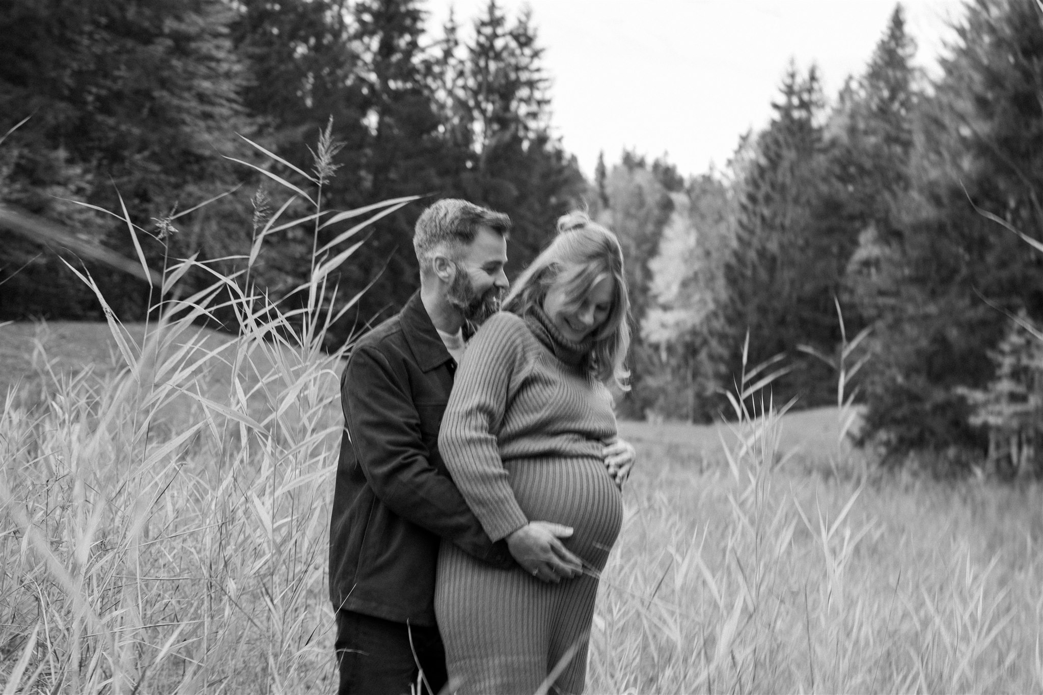Grainy Schwarzweißfoto eines schwangeren Paares im hohen Gras, der Mann hält den Babybauch der Frau