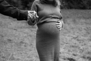 Schwarzweiß-Close-up einer Frau mit Hand auf dem Babybauch, während der Mann ihre Hand hält