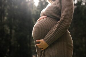 Close-up eines Babybauchs mit den Händen der Frau im Gegenlicht