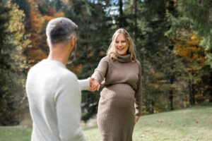 Mann hält die Hand seiner schwangeren Frau, während sie ihn lächelnd ansieht