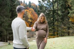 Mann hält die Hand seiner schwangeren Frau, während sie lächelnd auf ihn zugeht