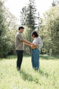 Pregnant couple standing opposite each other in a meadow while holding the baby bump