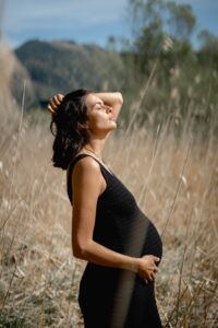 Side-view photo of a pregnant woman in golden grass holding her baby bump