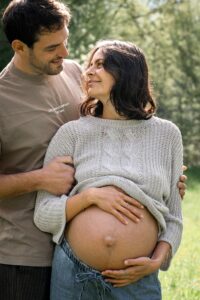 Man embracing his pregnant wife from behind while they look lovingly at each other
