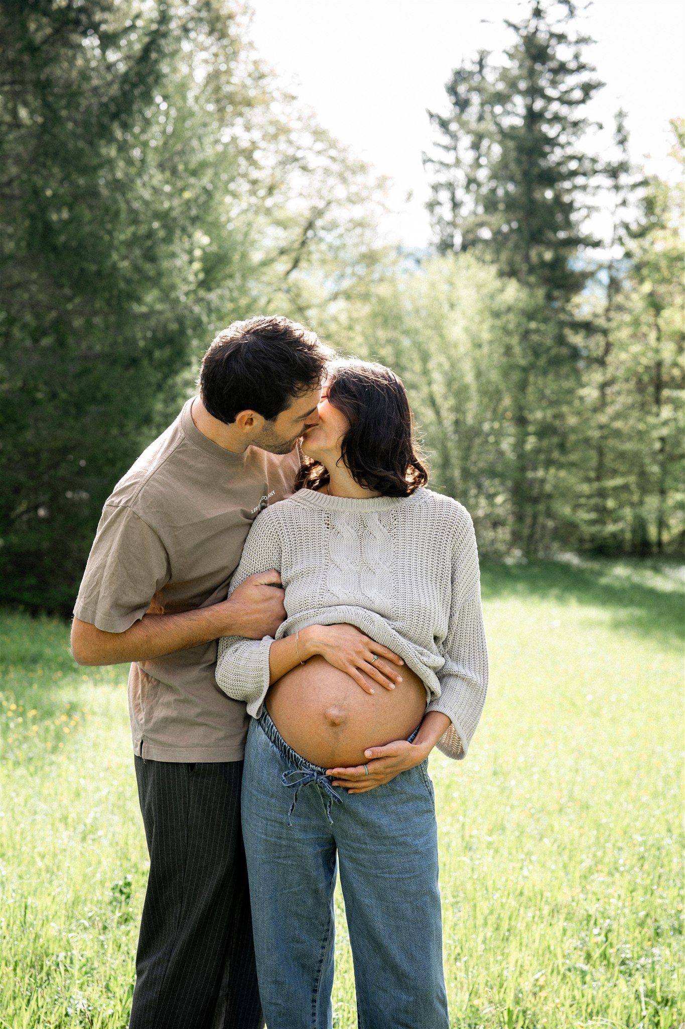 Pregnant woman holding her baby bump while her partner embraces and kisses her
