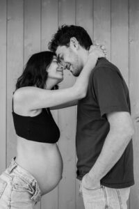 Black-and-white photo of a pregnant woman with her arms around her partner’s neck