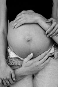 Black-and-white close-up of a baby bump framed by four hands