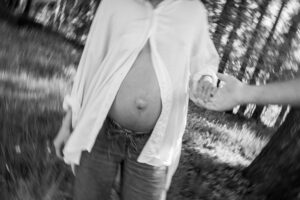 Black-and-white photo of a baby bump while the woman walks toward her partner wearing an open blouse
