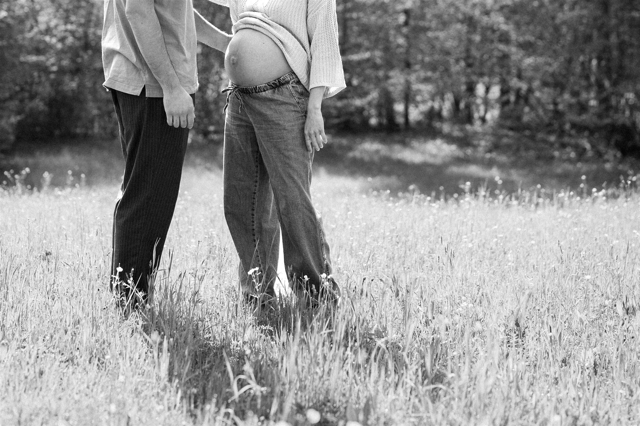 Cinematic black-and-white photo of a couple standing in a meadow with the baby bump visible