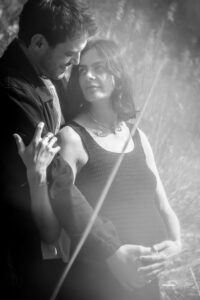 Vintage black-and-white photo of a pregnant couple standing in tall grass with their hands on the baby bump