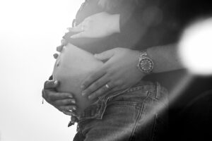 Vintage-Schwarzweiß-Close-up eines Babybauchs mit Lensflare und den Händen des Paares
