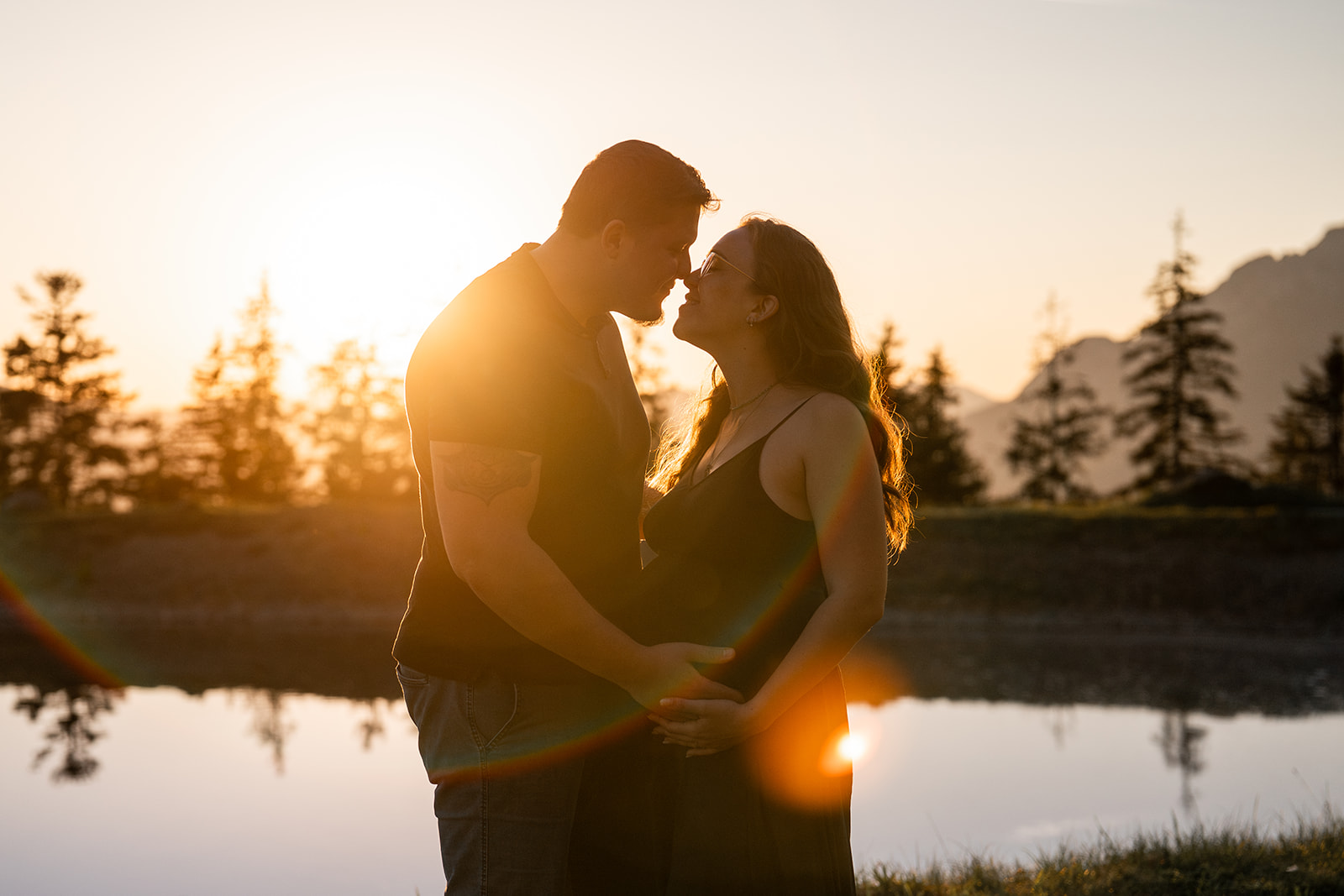 Vintage grainy photo of a pregnant couple by a mountain lake at sunset just before a kiss