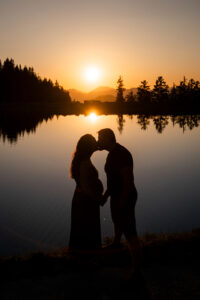 Hochformatiges Silhouettenfoto eines Paares beim Kuss vor Sonnenuntergang mit Spiegelung im See