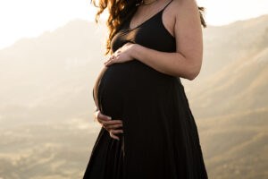 Close-up auf den Babybauch einer schwangeren Frau vor Sonnenuntergang in den Tiroler Bergen