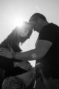 Schwarzweißfoto aus tiefem Winkel eines Paares mit Blick auf den Babybauch und Lensflare