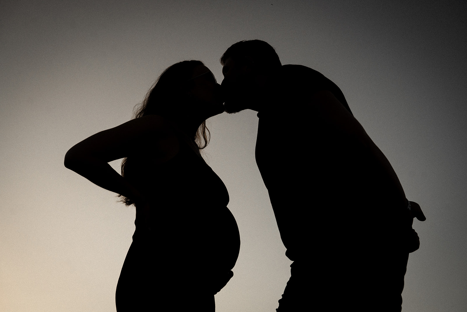 Low-angle silhouette photo of an expecting couple sharing a kiss