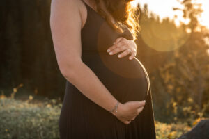 Close-up einer jungen Frau, die ihren Babybauch im goldenen Licht hält