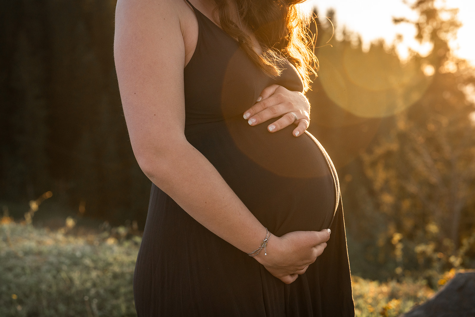 Close-up einer jungen Frau, die ihren Babybauch im goldenen Licht hält