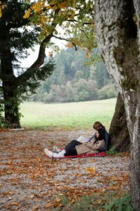 Young couple sitting beneath a tree on a picnic blanket while reading together