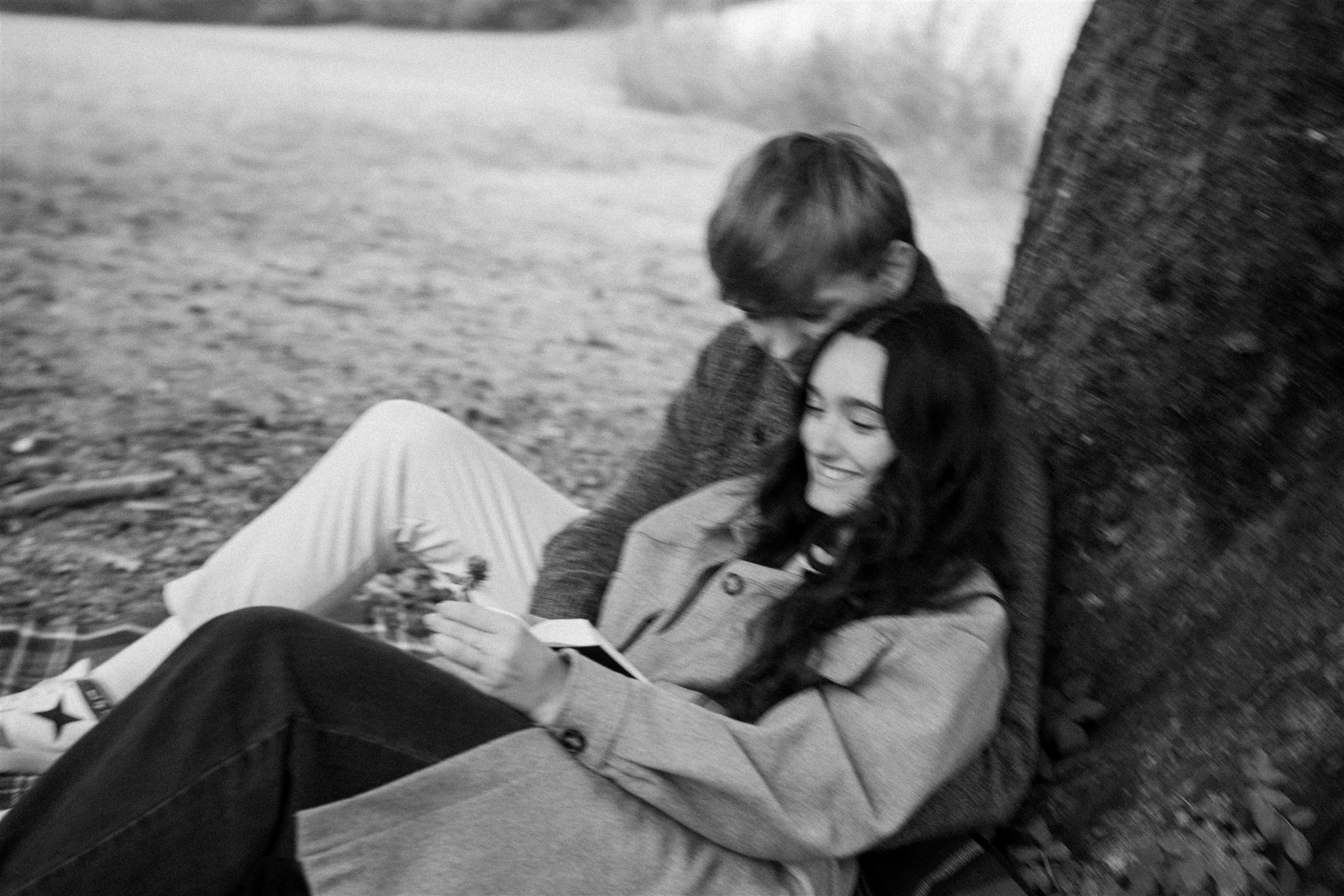 Cinematic photo of a young couple leaning against a tree while reading a book together