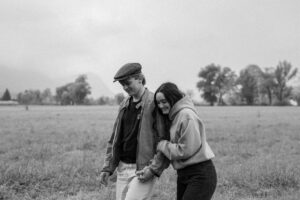 Black-and-white photo of a young woman holding onto her boyfriend’s arm while laughing